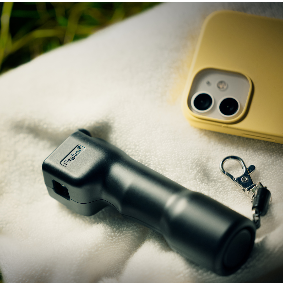 Image of a black Plegium Combo defence spray next to a smartphone. Lifestyle image.